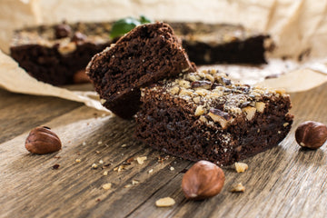 Dos trozos de brownie de chocolate con avellanas picadas apilados sobre una superficie de madera rústica.
