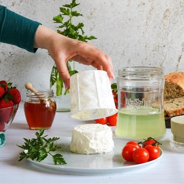 queso de kefir recien extraido de la cesta junto a tarro de cristal con suero de kefir