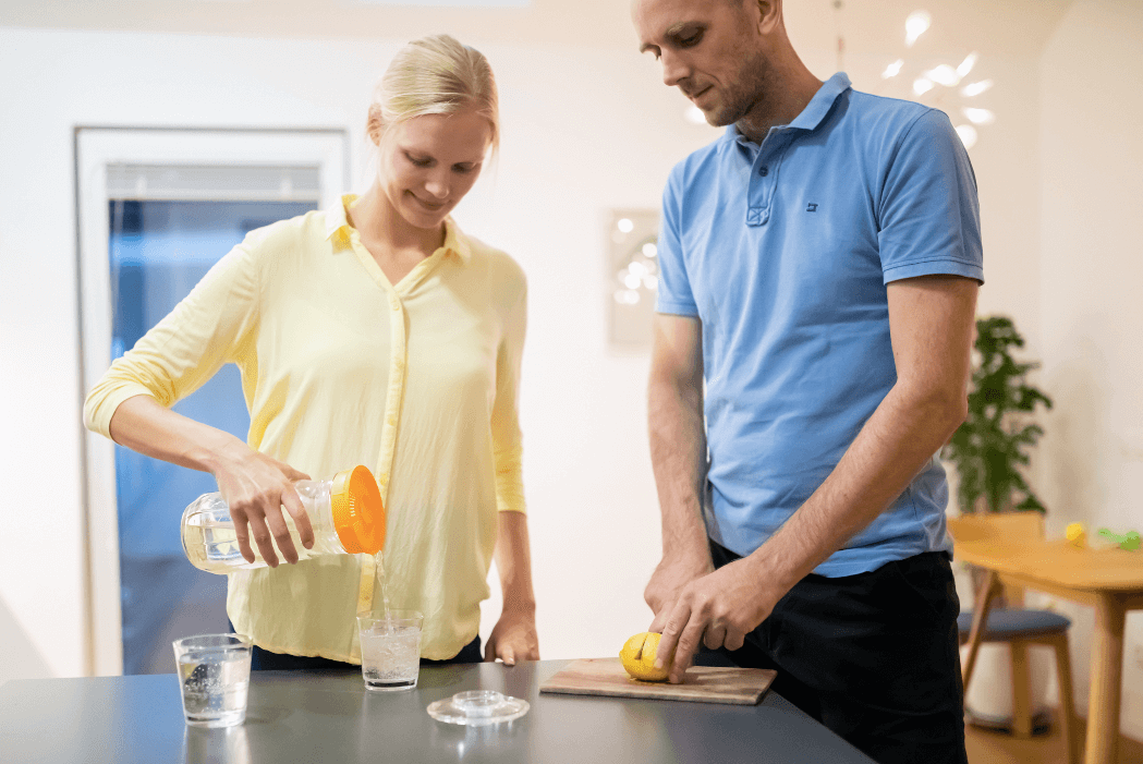 Mujer sirve agua de una jarra y un hombre corta un limón, preparando una bebida para un detox digestivo.