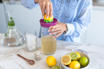 Una persona exprime un limón en un tarro de vidrio con kefir de agua para preparar una bebida detox de primavera.