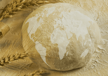 Masa de pan con un mapamundi de harina y espigas de trigo, representando los panes del mundo sobre una base enharinada.