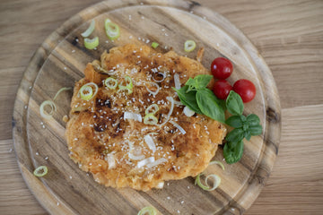Tortitas de kimchi caseras en una tabla de madera, adornadas con sésamo, cebolleta, tomates cherry y albahaca.