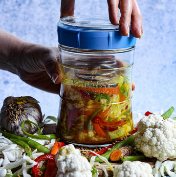 Manos preparando fermentos caseros en un tarro de vidrio Kefirko rodeado de verduras frescas