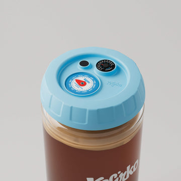 Vista superior del tarro de vidrio Kefirko con tapa azul que incluye un reloj de fermentación y un termómetro.