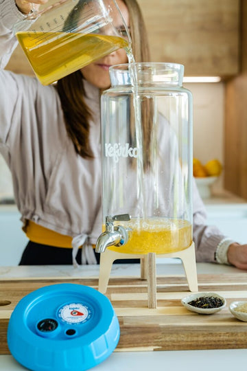 Persona vertiendo líquido de una jarra medidora en el tarro de vidrio Kefirko para hacer kombucha en una cocina.