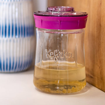 Tarro de vidrio Kefirko con tapa fucsia, lleno de kéfir de agua y con los gránulos asentados en el fondo.