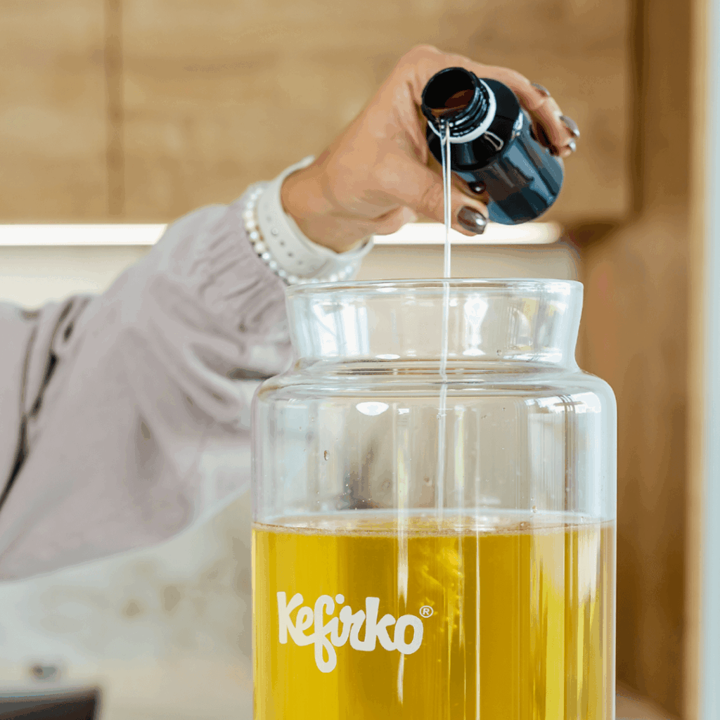 Mano añadiendo el cultivo de kombucha líquido de una botella a un tarro de fermentación Kefirko.