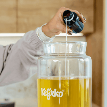 Mano añadiendo el cultivo de kombucha líquido de una botella a un tarro de fermentación Kefirko.