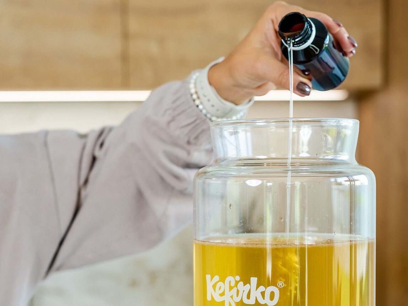 Mano añadiendo el starter a un tarro de vidrio Kefirko con té dulce para la kombucha casera.